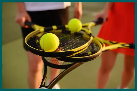 Deux joueurs de tennis tenant des raquettes avec des balles neuves sur un court extérieur, se préparant pour un match ou une séance d'entraînement en plein jour.