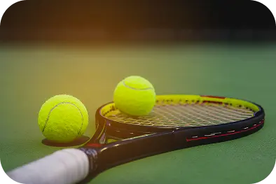 Gros plan sur une raquette de tennis avec deux balles jaunes posées sur un court vert, symbolisant l'entraînement professionnel et l'équipement sportif.